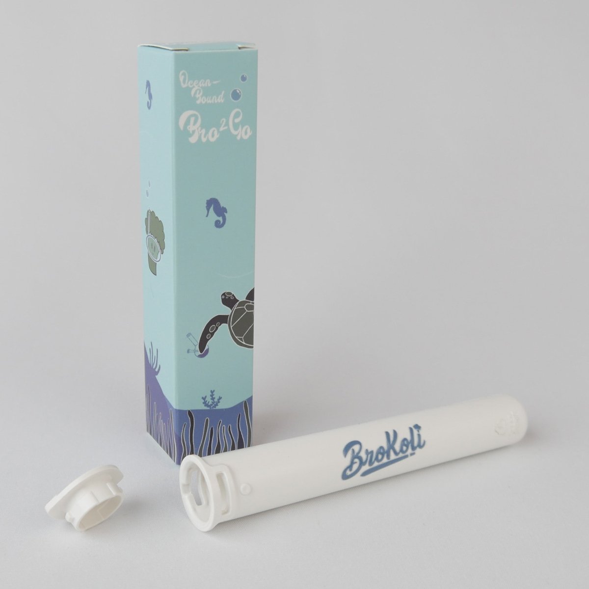 Das Ocean-Bound Bro2Go von BroKoli, ein weißes, kindersicheres Transport-Case für Joints aus recyceltem Ocean-Bound Plastic. Neben dem geöffneten Case steht die Verpackung mit maritimem Design, das eine Meeresschildkröte, Seepferdchen und Unterwasserpflanzen zeigt.