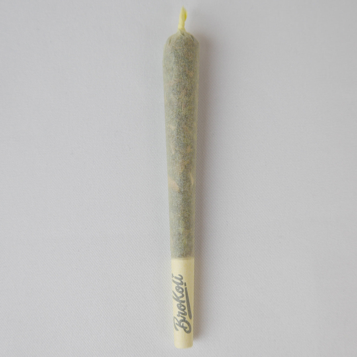Ein gefüllter Colored KoliCone in der Farbe Yellow Mellow liegt auf weißem Hintergrund. Der Cone hat einen gelben Filter mit BroKoli-Logo und ein leicht transparentes Paper, durch das der Inhalt sichtbar ist. Das obere Ende ist eingedreht.
